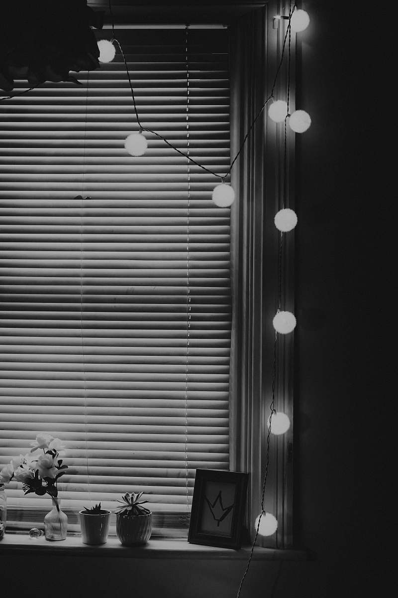 indoors turned on string lights beside blinds black-and-white